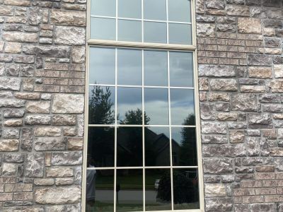 Stone house wall with a tall reflective window showing trees and sky