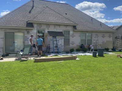 Workers painting the exterior of a beige house with a steep roof and green lawn.