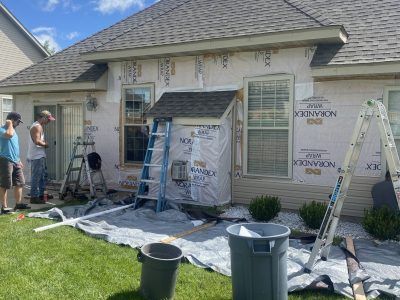 Workers and ladders around a house under exterior renovation with tarps and siding materials