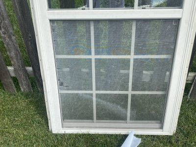White window screen leaning against a fence on grass outdoors