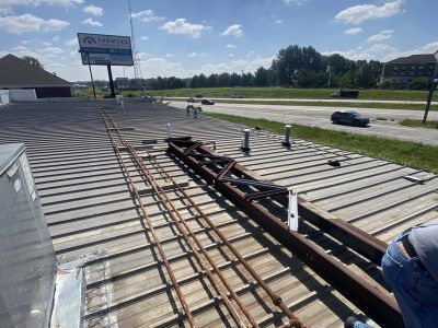 Roof under construction with exposed beams and workers near a roadside parking lot
