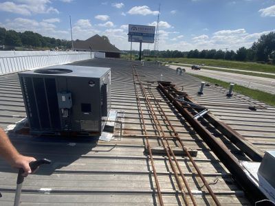 Roof workers installing HVAC units and conduit on a flat commercial roof under a clear sky