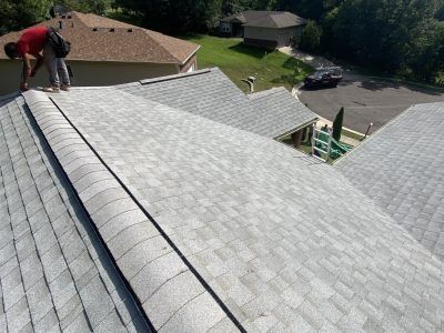Worker on a shingled roof during roof installation, overlooking a residential neighborhood.