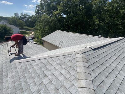 Person installing roof shingles on a gray rooftop in a sunny residential area