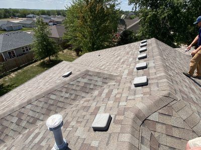 Rooftop with gray shingles and vents, viewed from above, with a worker at the right edge.