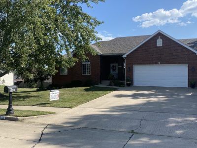 Brick suburban house with two-car garage, driveway, lawn, and large tree by the street