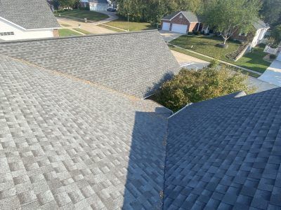 Residential rooftops with gray shingles, trees, and neighboring houses in a suburban neighborhood