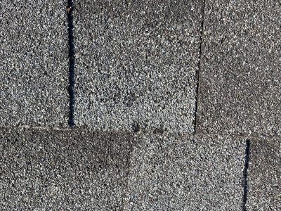 Close-up of gray asphalt shingles with dark vertical seams and a horizontal overlap line