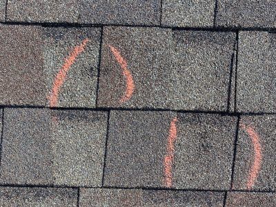 Gray roof shingles with orange spray-painted markings on several tiles