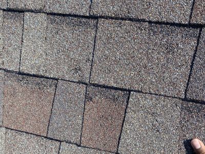 Close-up of gray and brown roof shingles with a person’s hand at the bottom right