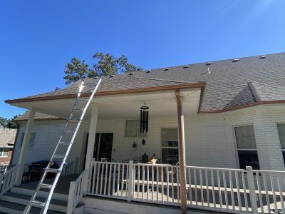 Ladders leaning against a white house roof above a covered porch under a blue sky