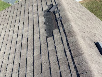 Shingled roof with a damaged section and missing shingles near the ridge