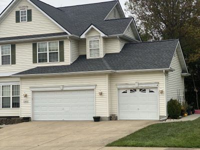 Suburban house with two garages, light siding, and a driveway in front