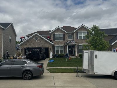 Suburban house with open garage, parked car in driveway, and white trailer on the street under cloudy sky
