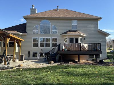 Suburban house with large arched windows and a raised back deck in a grassy yard under a clear blue sky