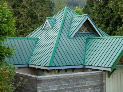 Green metal roof with multiple gables on a concrete building amid trees