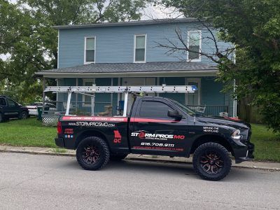 Black service truck with ladders parked in front of a blue house