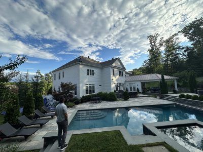 Backyard pool and patio beside a white two-story house under a cloudy sky