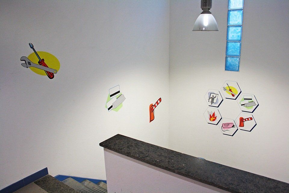 Una tromba delle scale con pareti decorate con icone dipinte di attrezzi, simboli di sicurezza e una barriera rossa per il traffico.