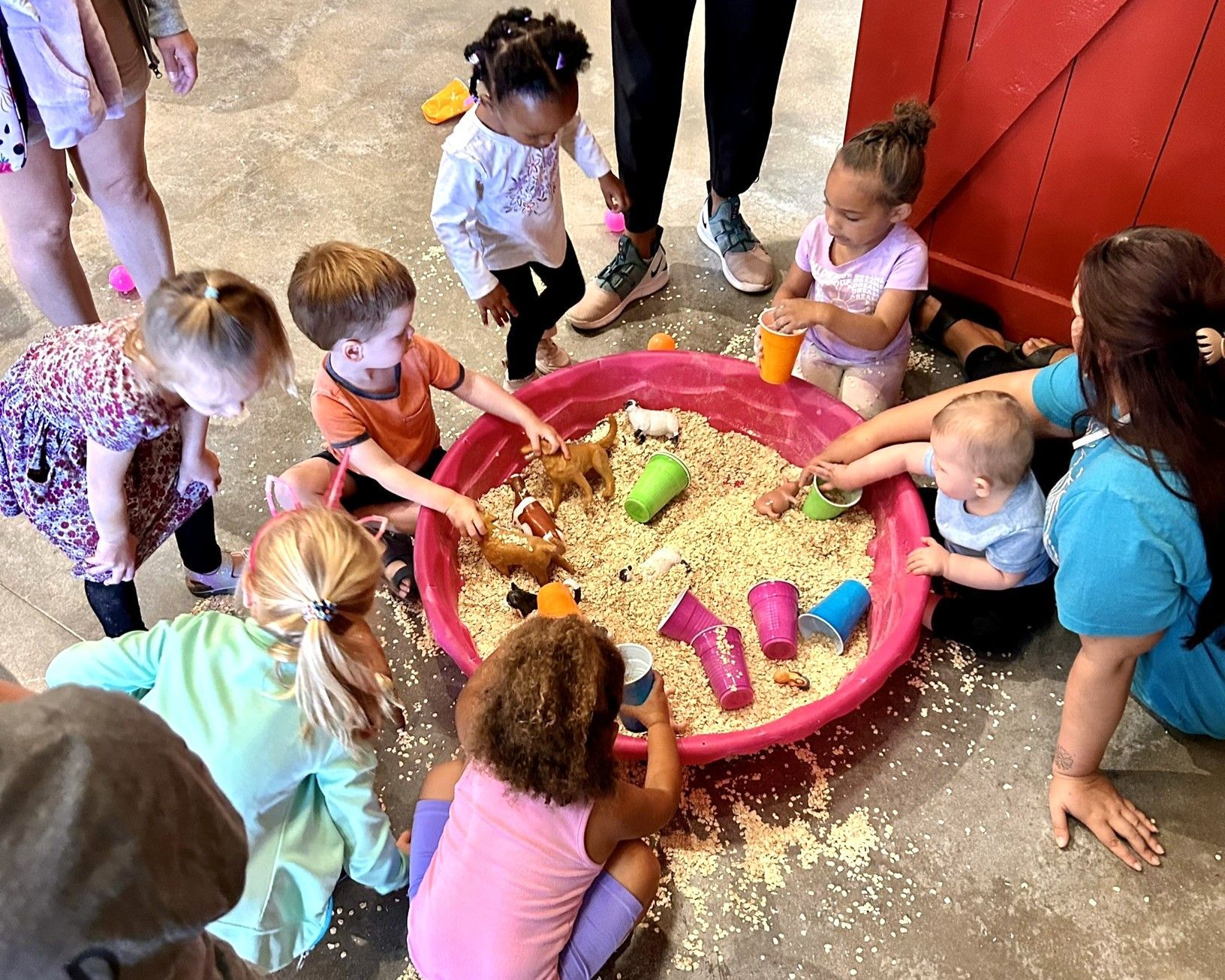 Children playing together around a large pink sand tray indoors, using colorful toys.