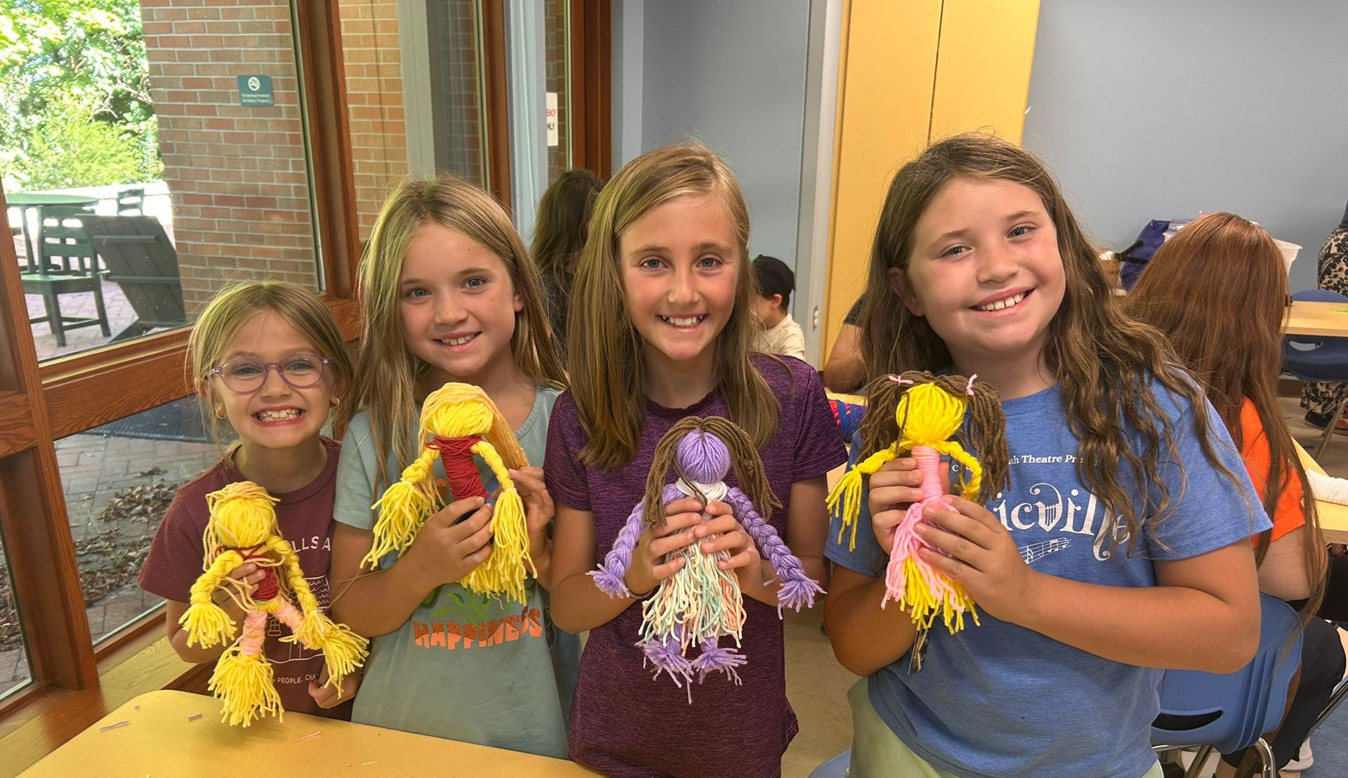 Four children smiling and holding small dolls in a bright room