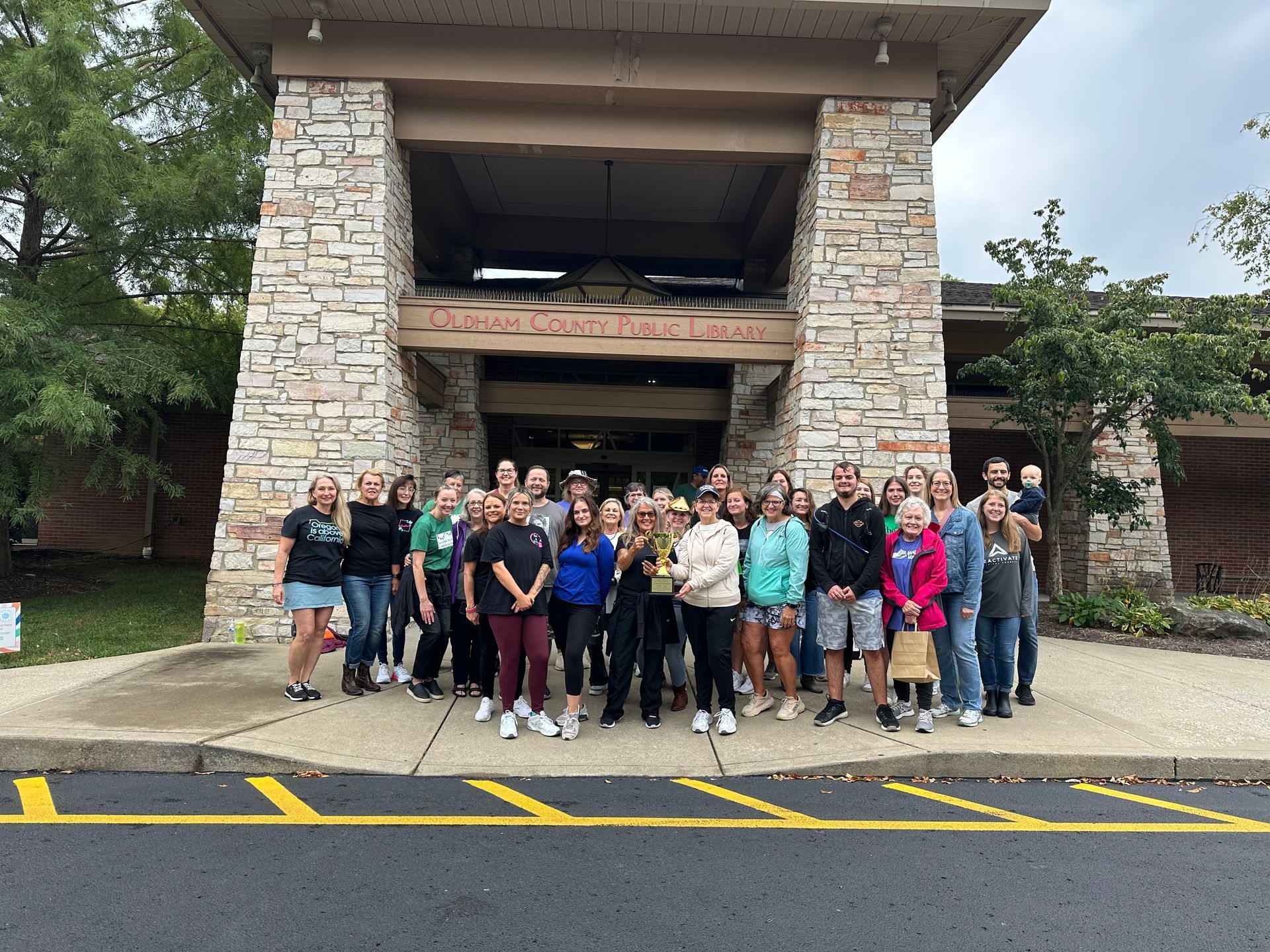 Group of people posing in front of a stone building with an open upper level and yellow road markings.