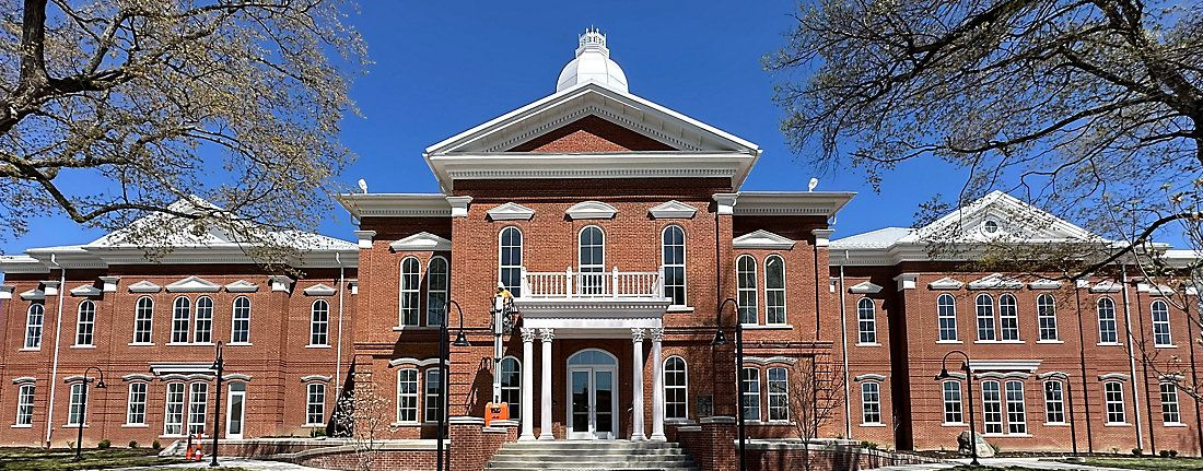 Brick civic building with white columns, American flags, and landscaped entrance under a blue sky