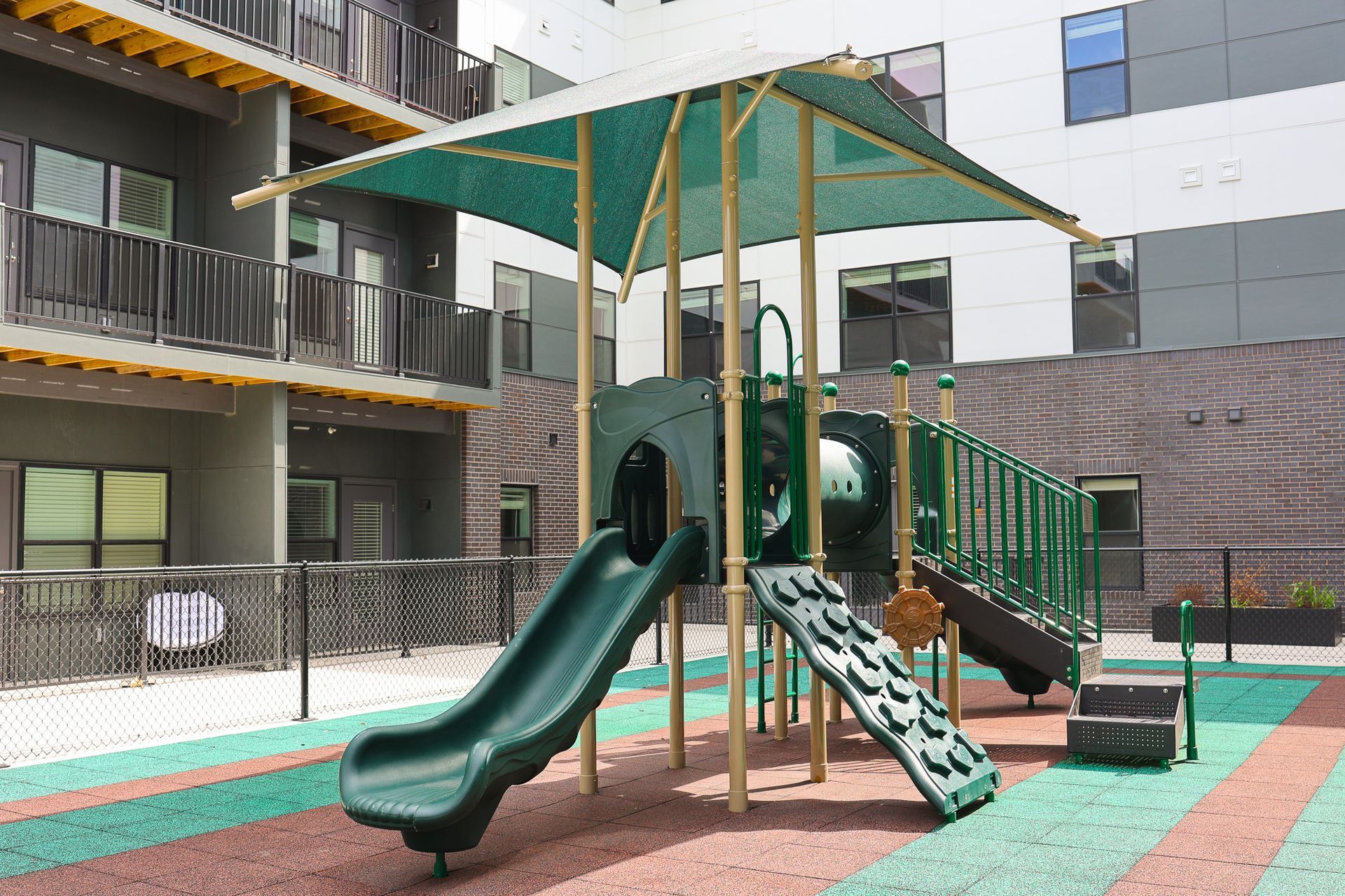 ADA Friendly Apartments in Downtown Lincoln, NE - Union at Antelope Valley - Outdoor Playground With Green Slides, Climbing Features, Shade Canopy, and Rubber Surface Flooring.