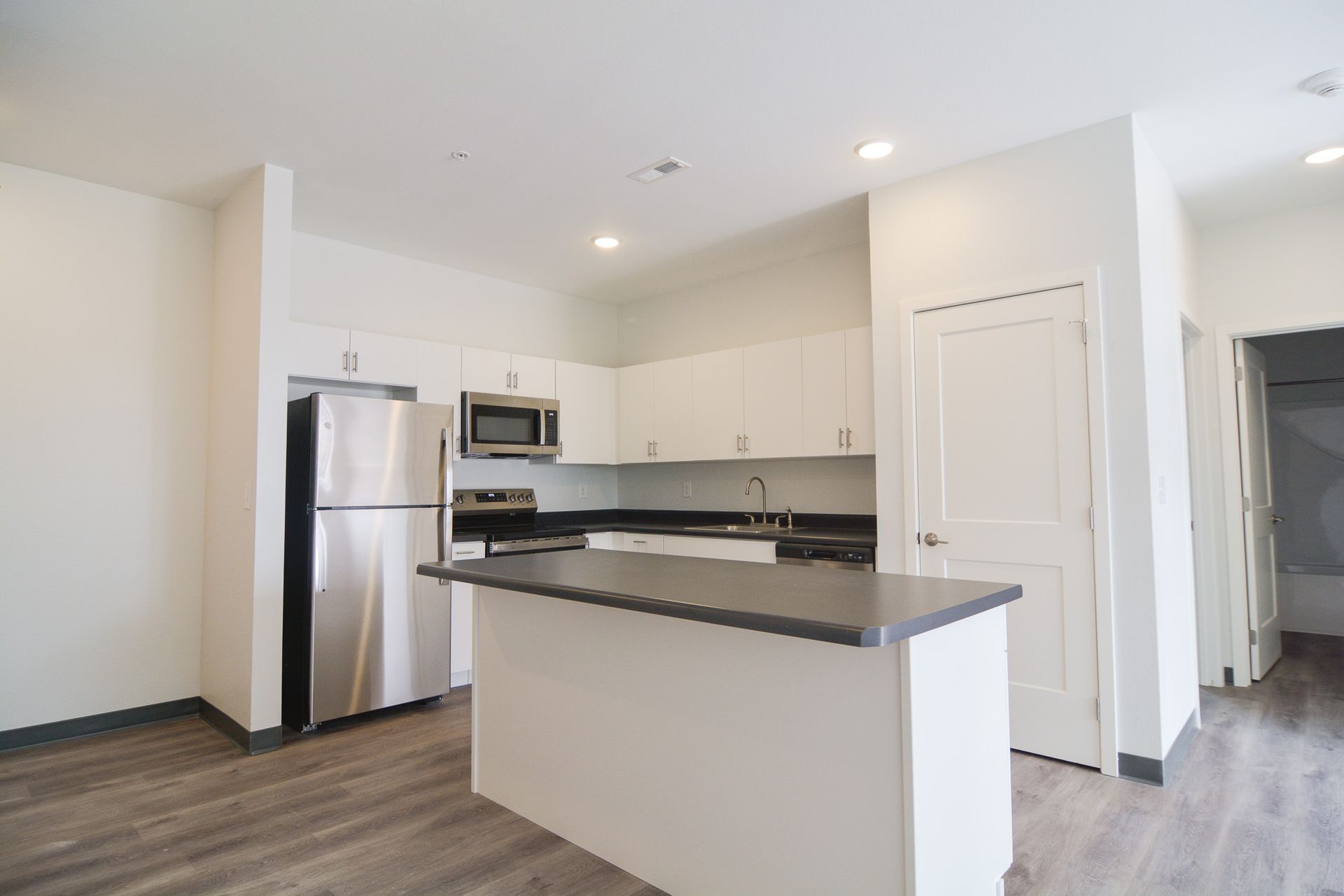 Downtown Lincoln, NE, Pet-Friendly Affordable Apartments - Union at Antelope Valley - Kitchen With Stainless Steel Appliances, Dark Countertops, And Wood Style Flooring.