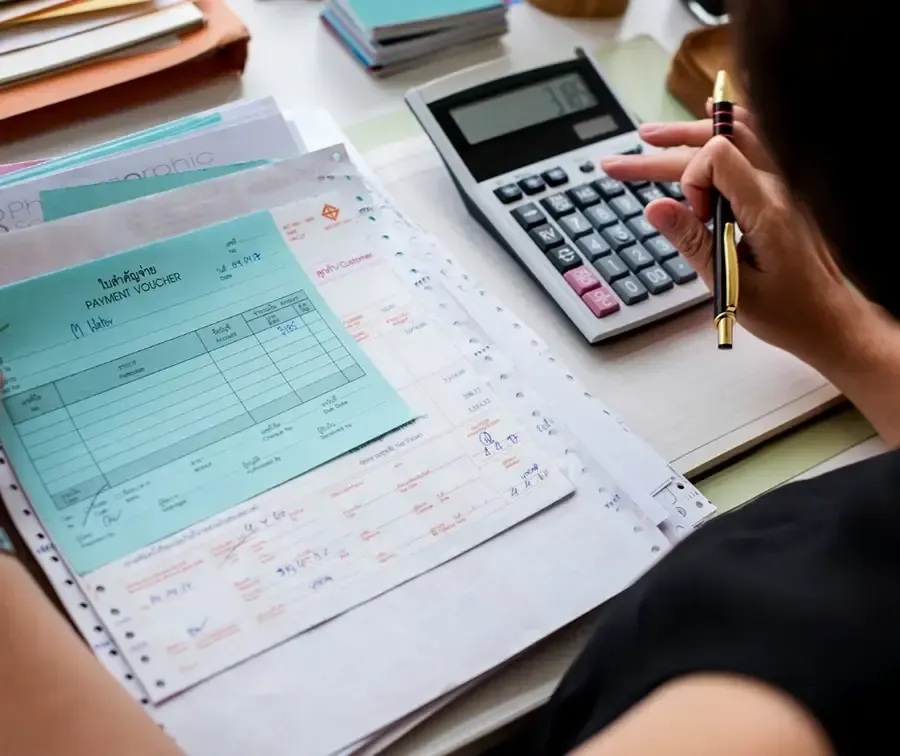 a woman is sitting at a desk using a calculator and a pen .