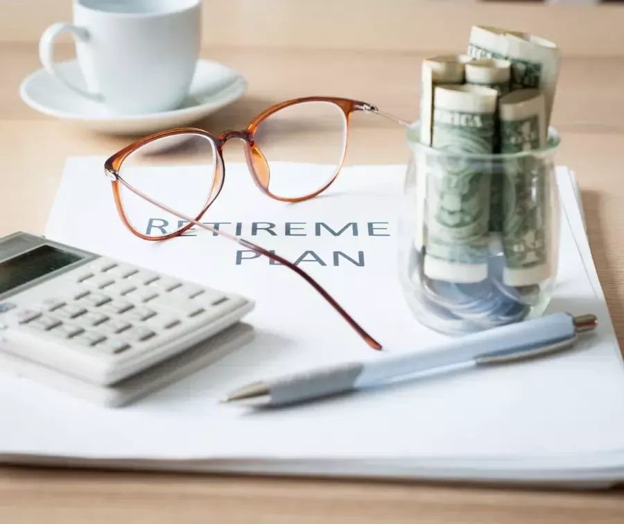 Retirement Plan documents with jar of money, calculator, a pen, and eyeglass on it.