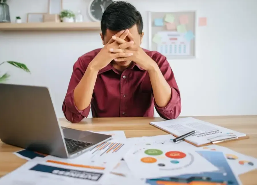A man is sitting at a desk with his hands on his face.