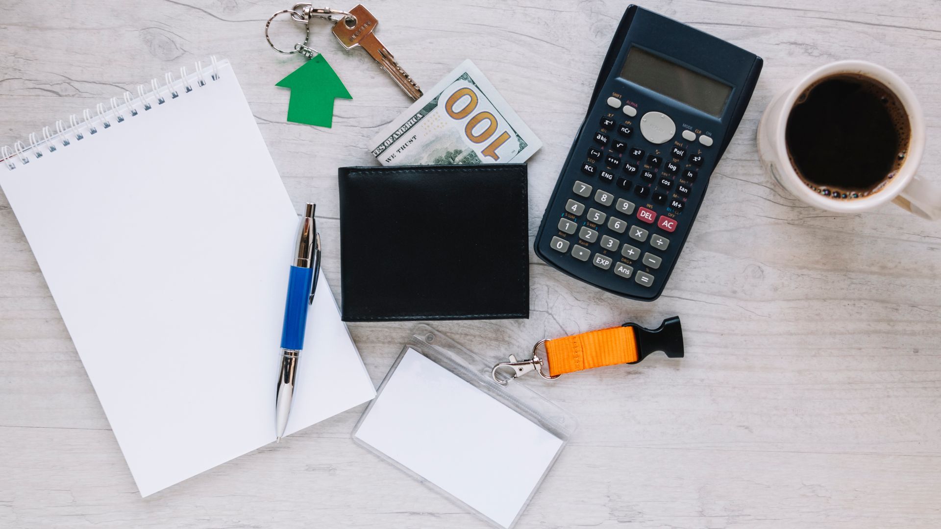 A table with a calculator , wallet , pen , keys , and a cup of coffee.