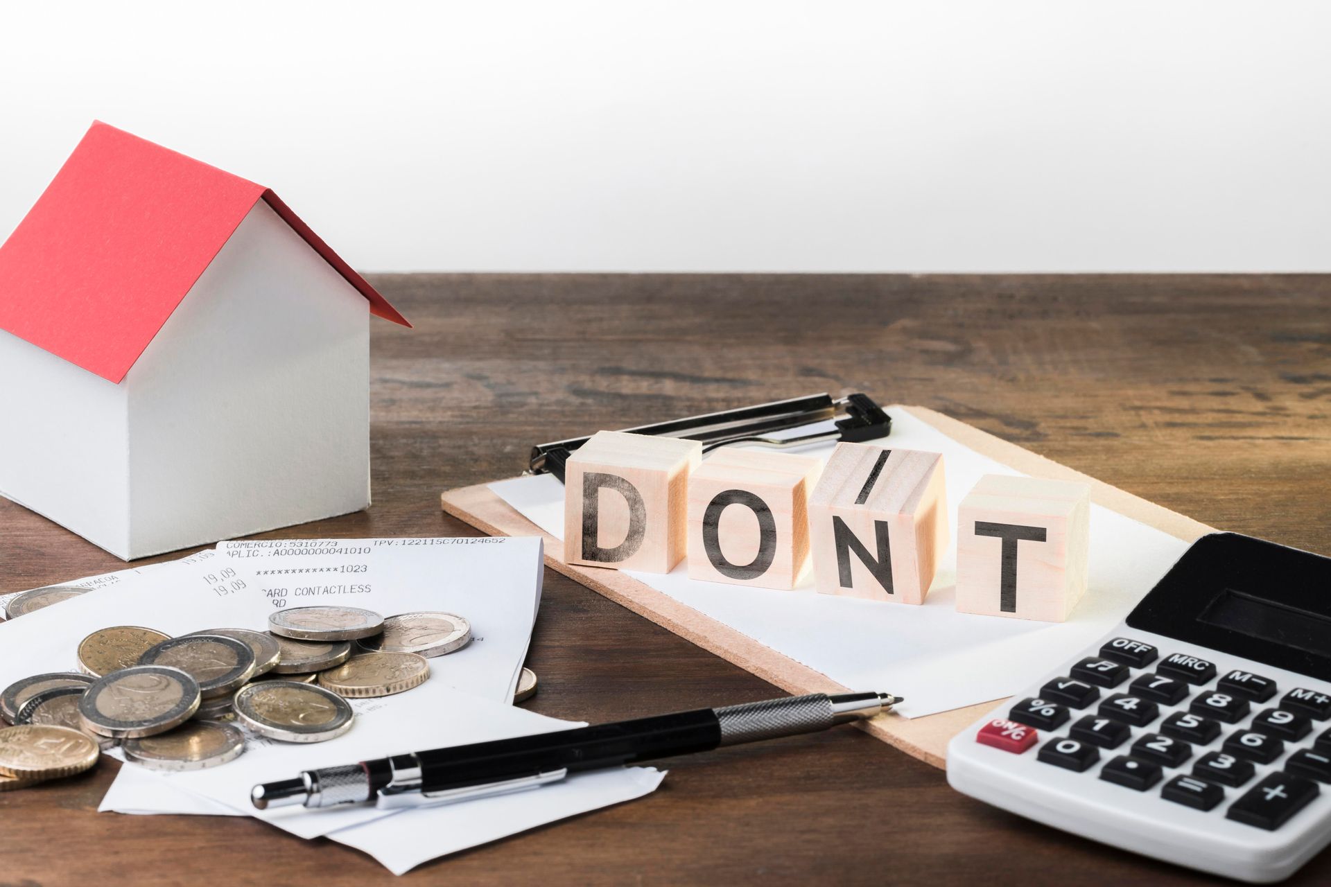 A wooden table with a house , coins , a pen , and a calculator.