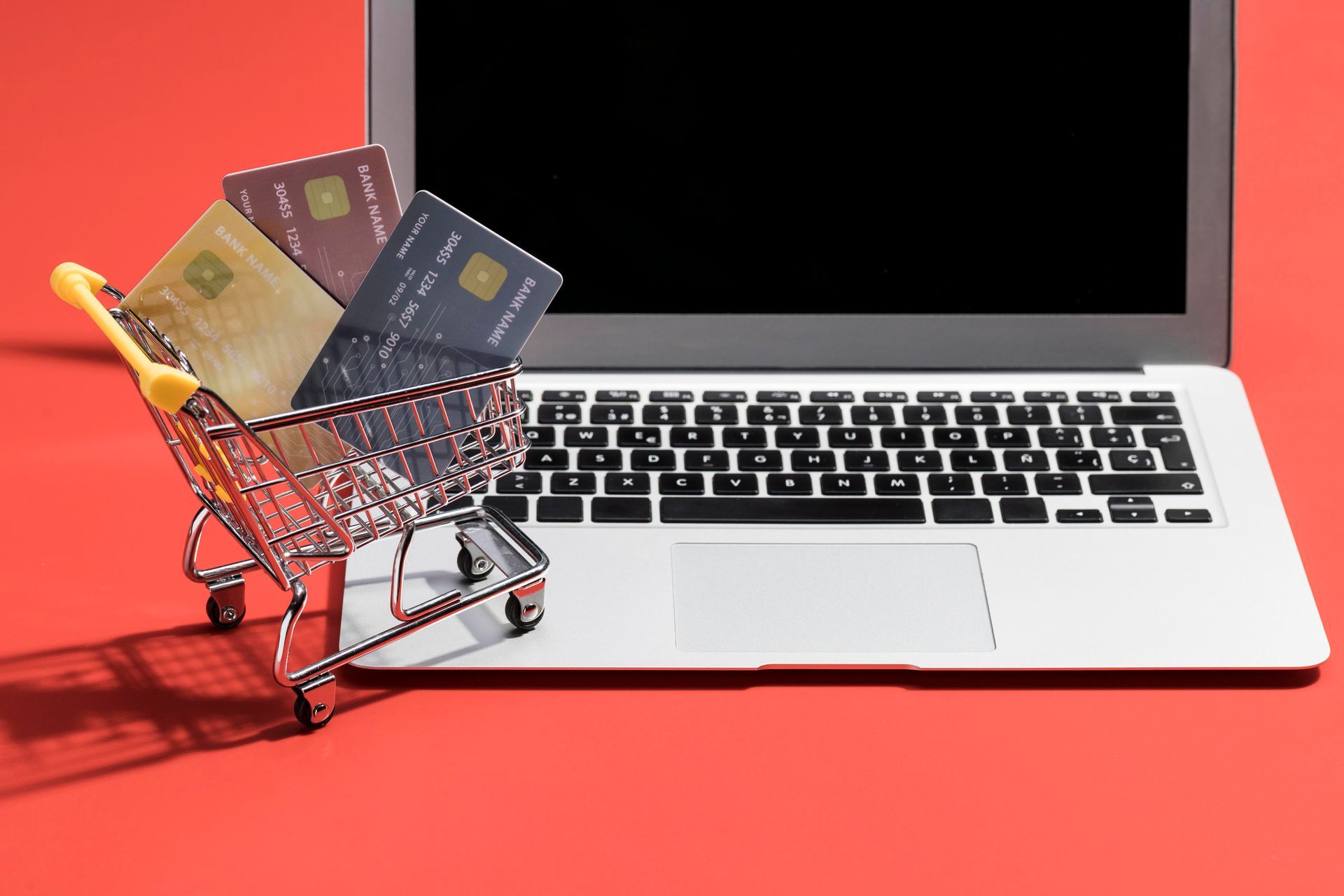 A shopping cart filled with credit cards is sitting on top of a laptop computer.