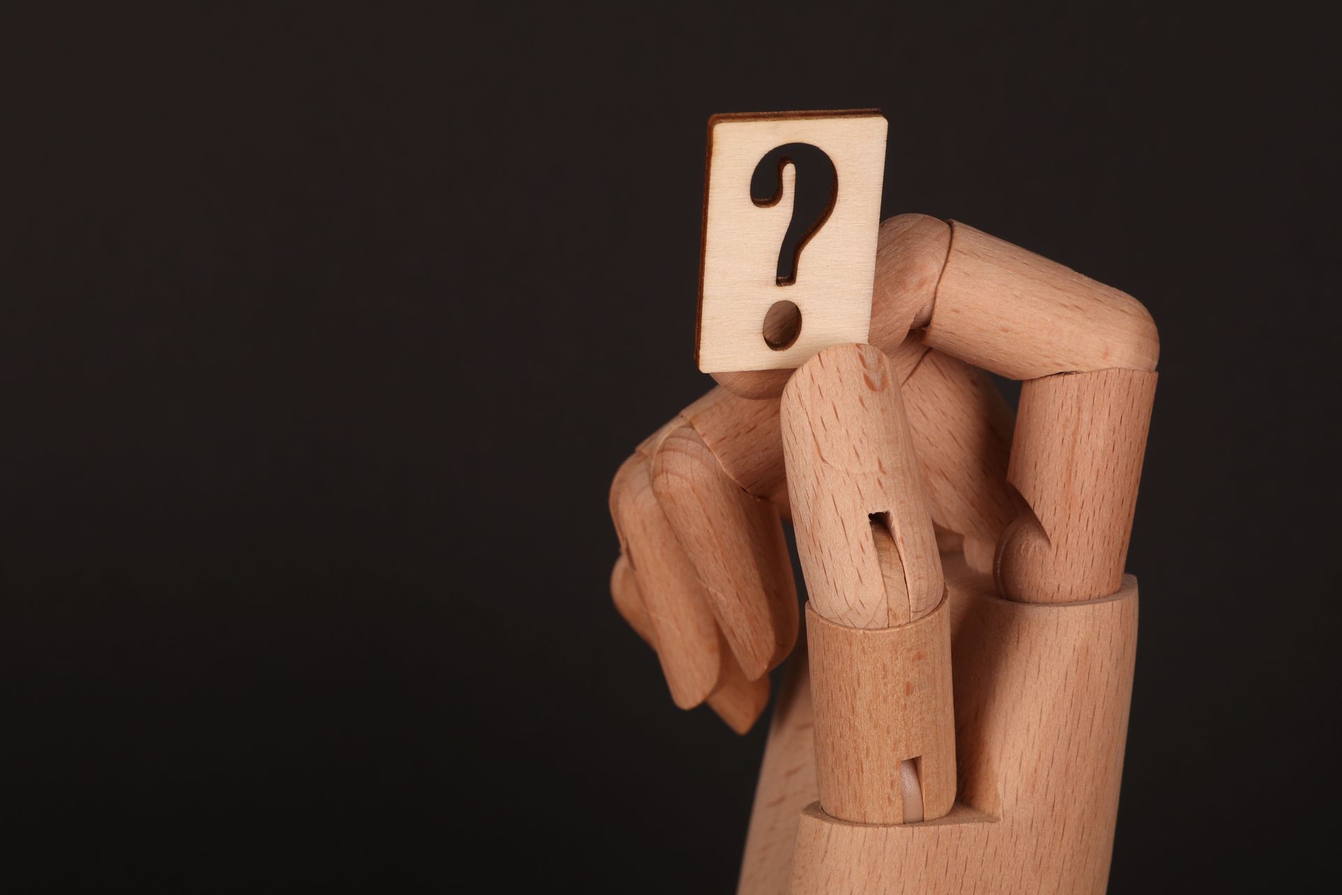 Wooden mannequin holding a card with a black question mark on a dark background