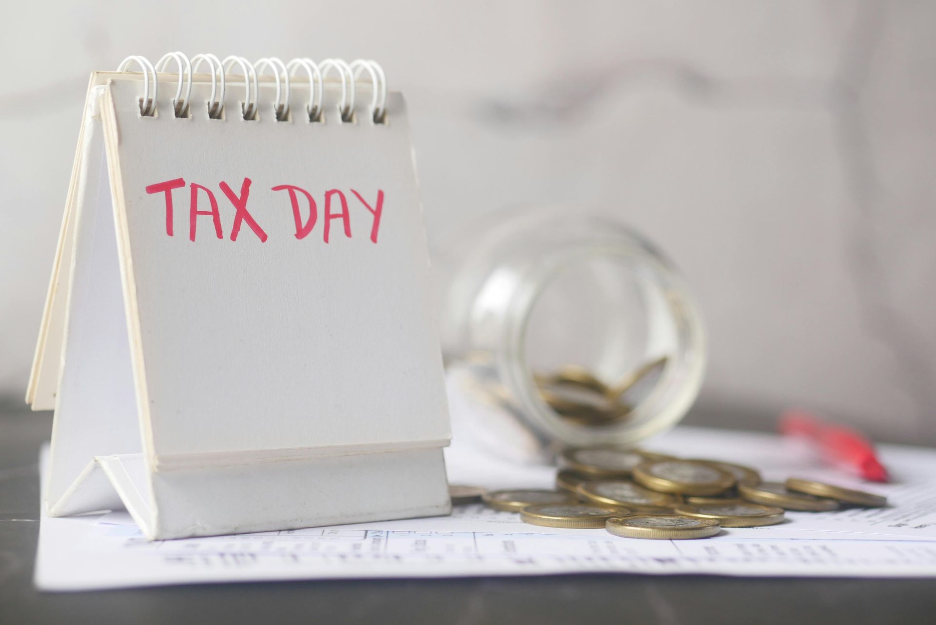 Desk calendar labeled “TAX DAY” beside scattered coins and a magnifying glass
