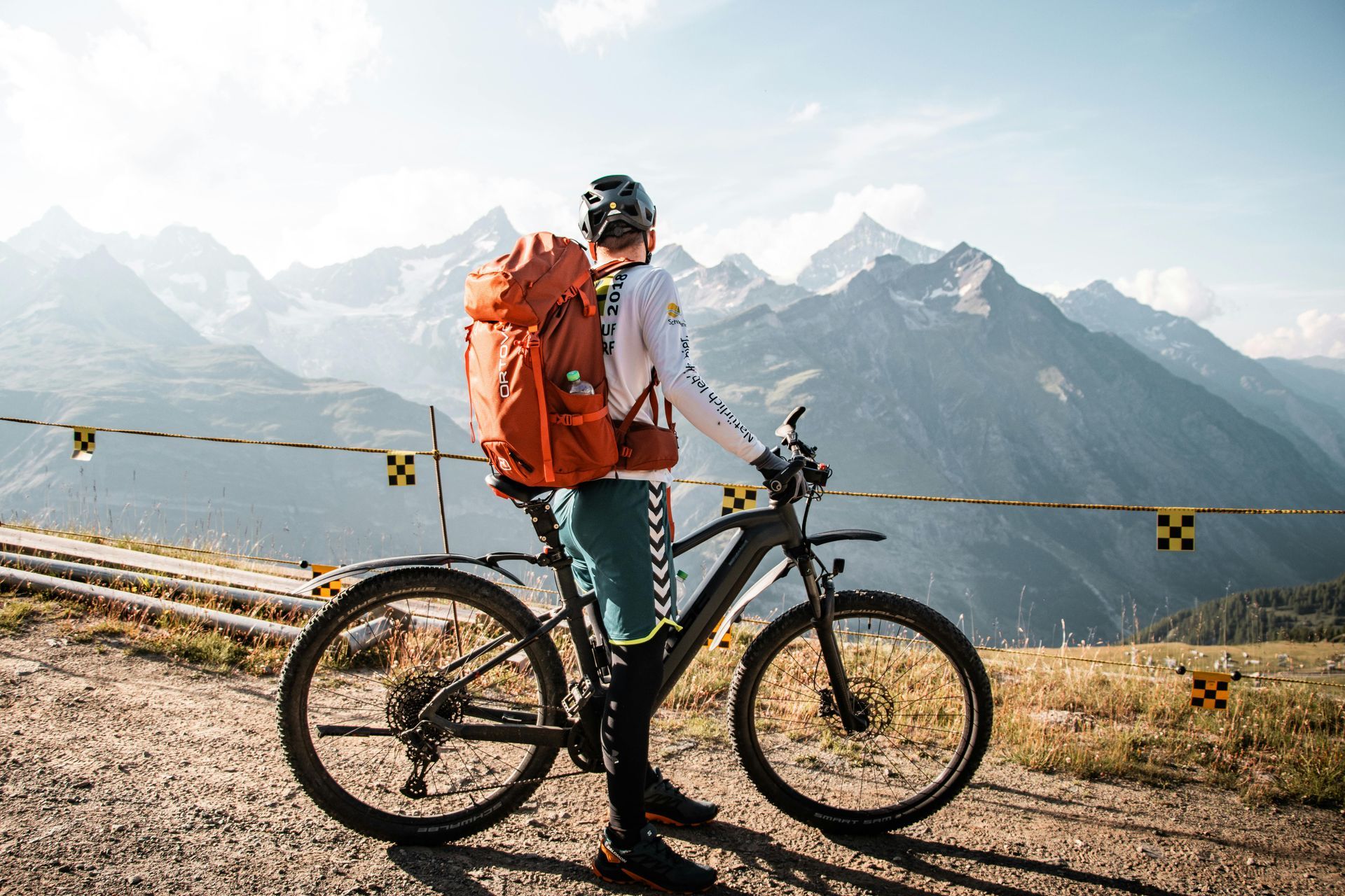 Person with backpack on mountain bike, admiring mountain view.
