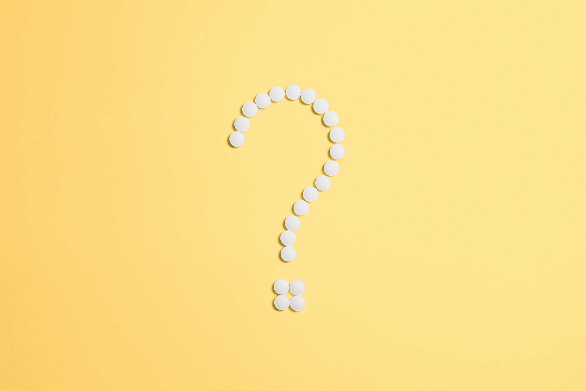 A question mark made of white pills on a yellow background.