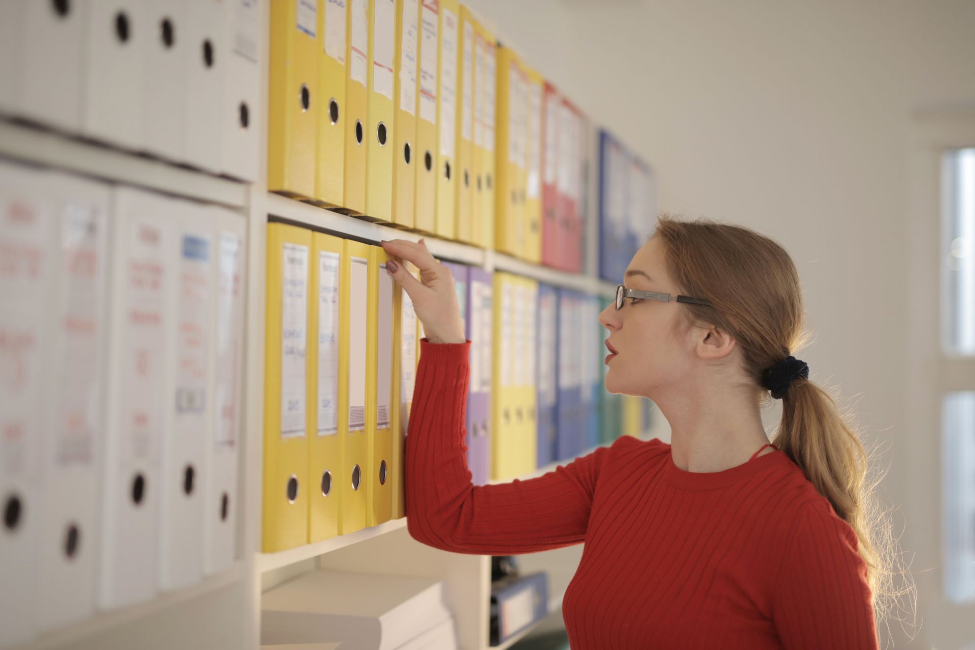Woman in red sweater reaching for a file on a shelf in an office archive