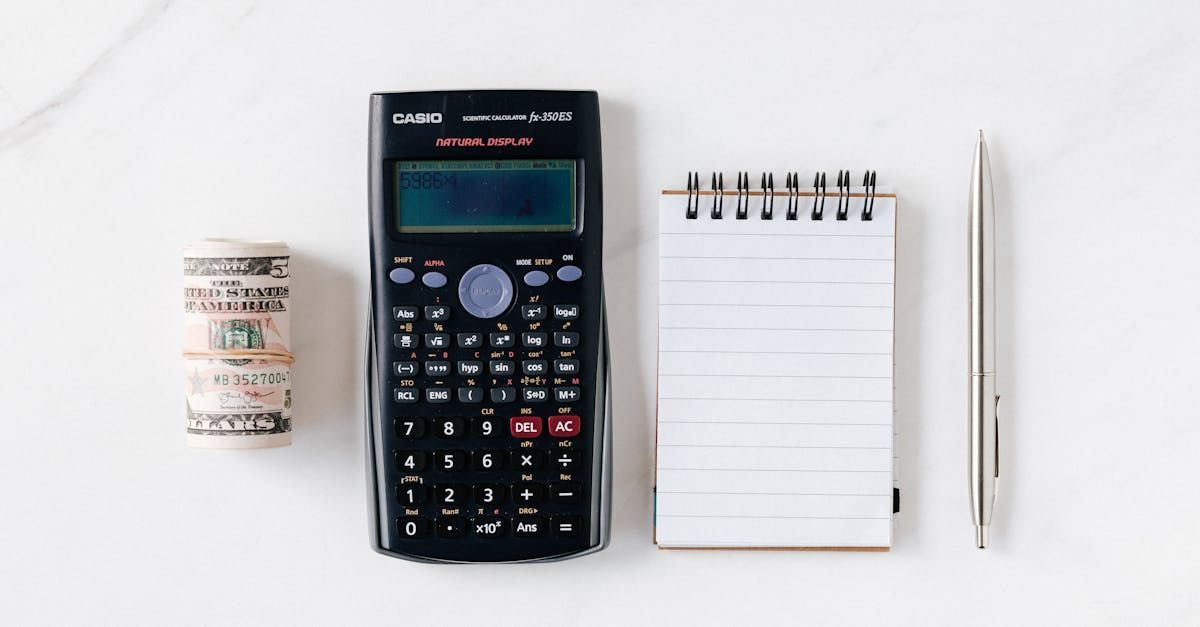 A calculator , a notebook , a pen , and a roll of money are on a table.