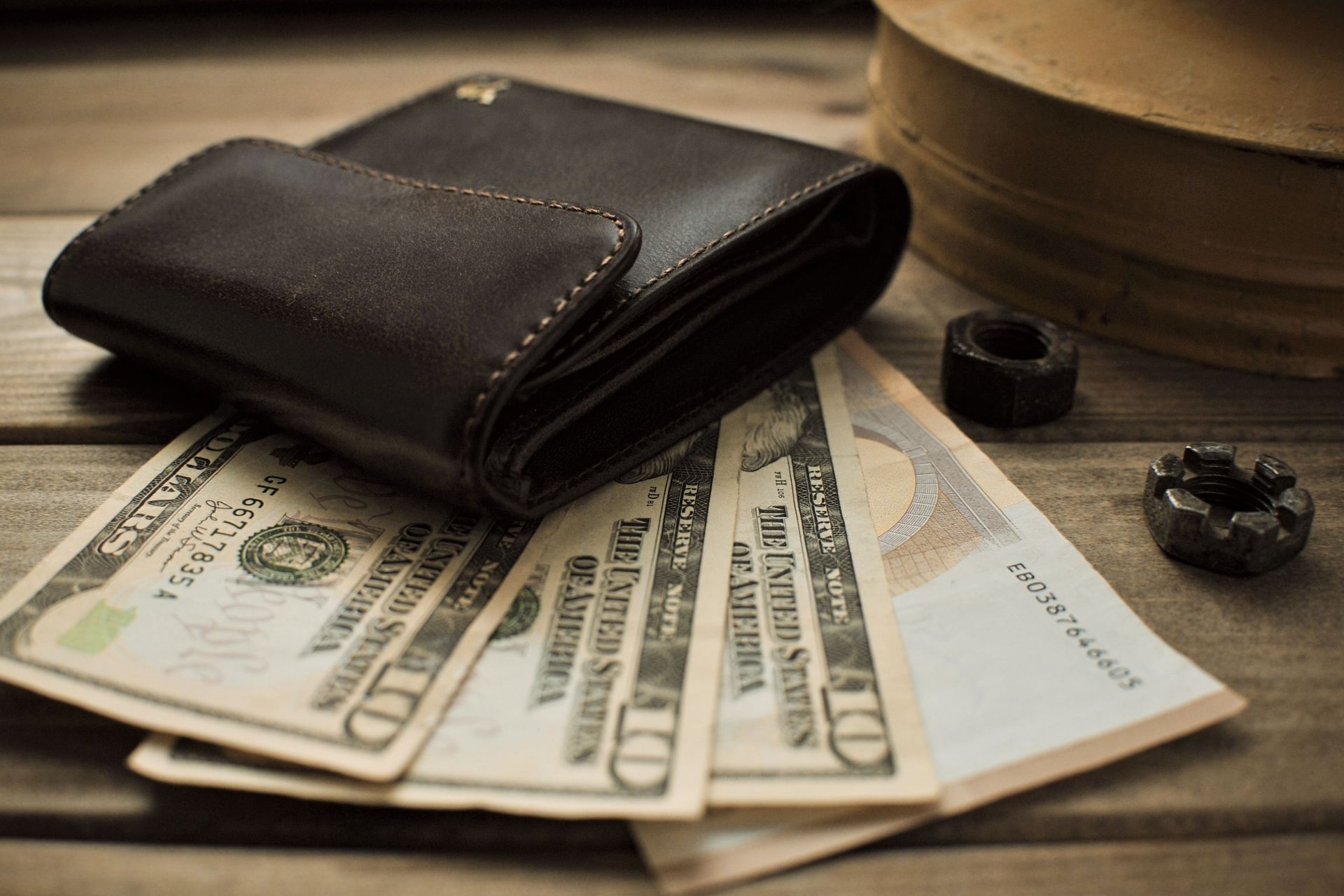 Black wallet with US dollar bills on a wooden table, with two rings nearby