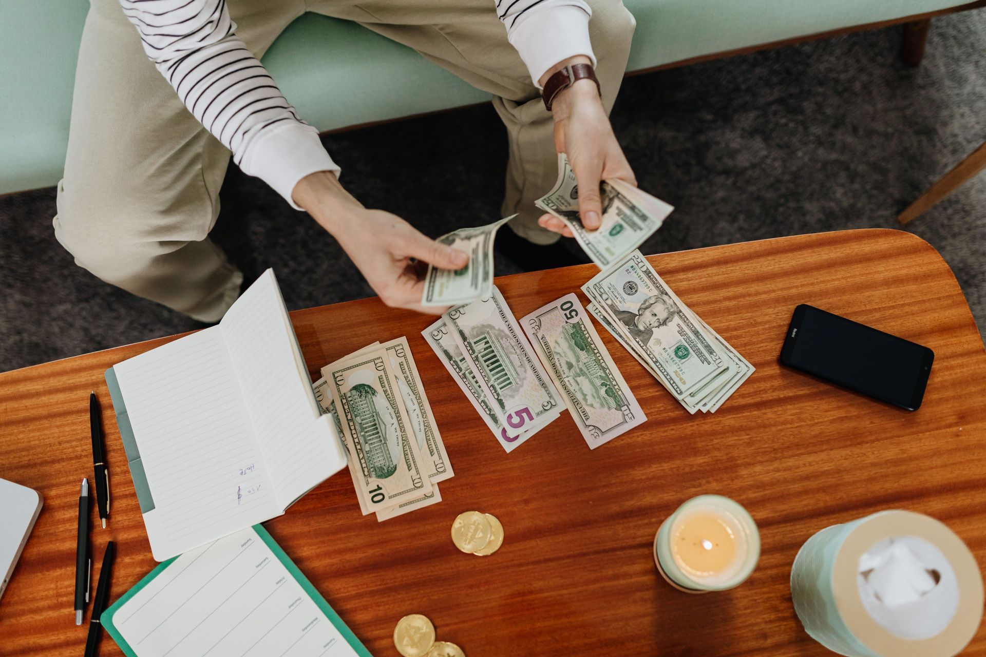 Hands counting cash on a wooden table with a notebook, smartphone, and coffee cup