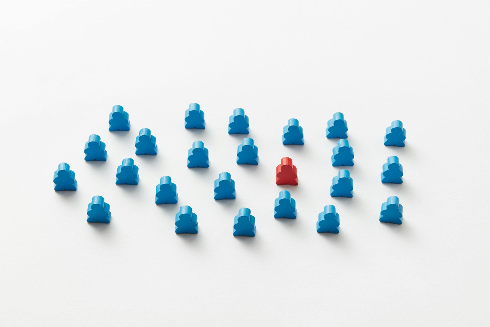 Blue and red wooden figures on a white background; one red figure stands out amidst many blue ones.