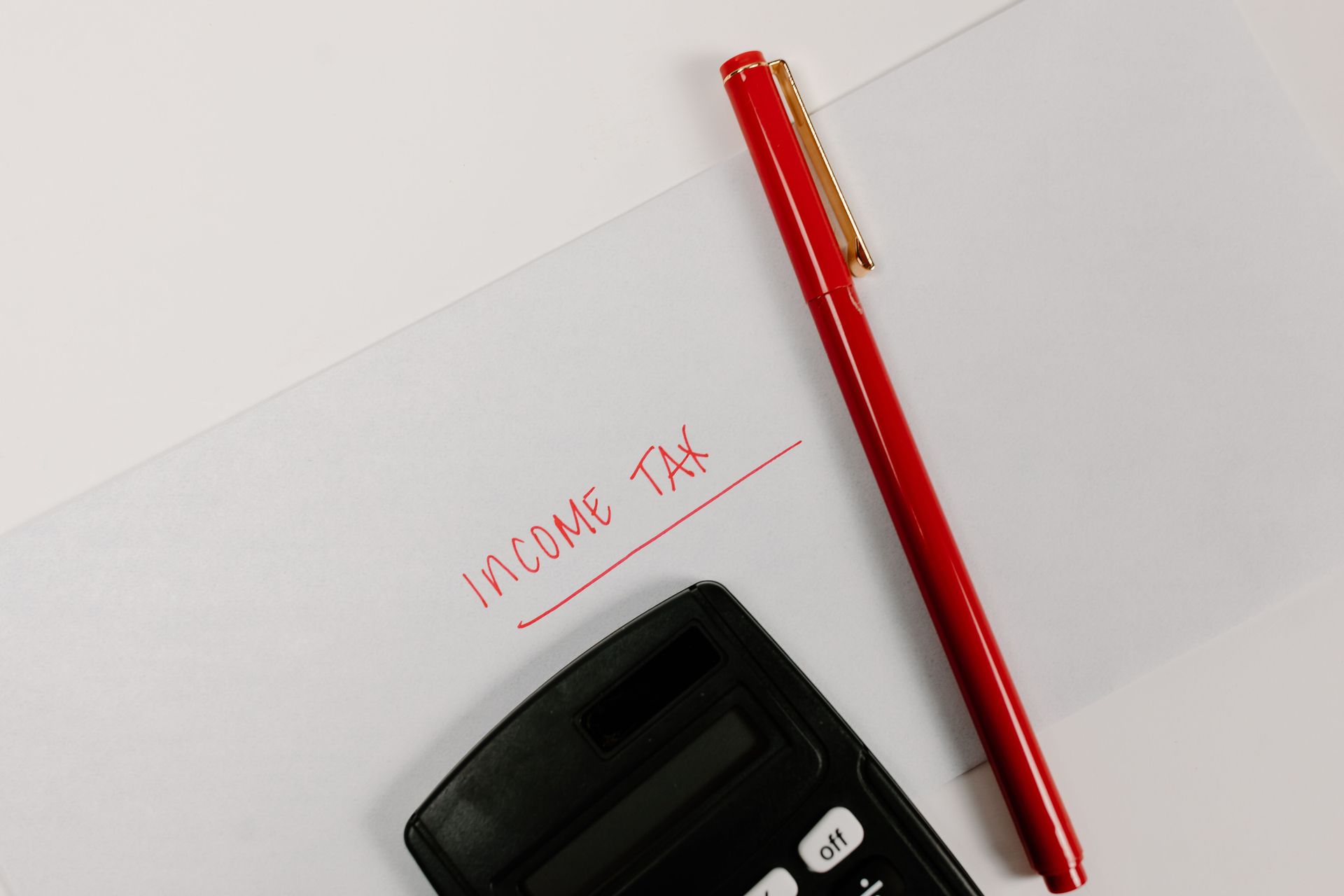 Red pen, calculator, and handwritten “income tax” on paper.