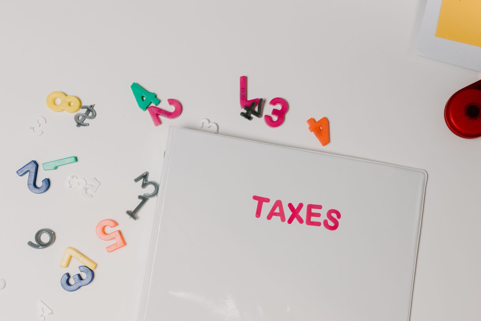 Paper with “TAXES” on white desk surrounded by colorful scattered numbers and symbols