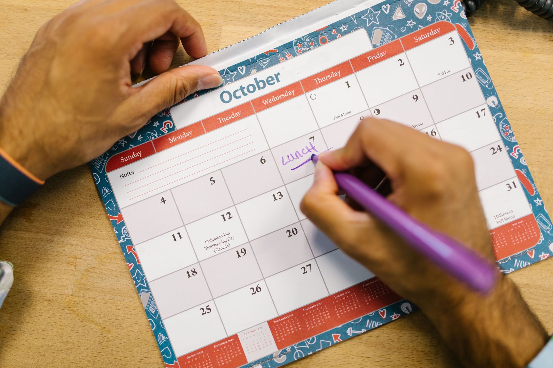 Hands writing on an October wall calendar with a purple pen