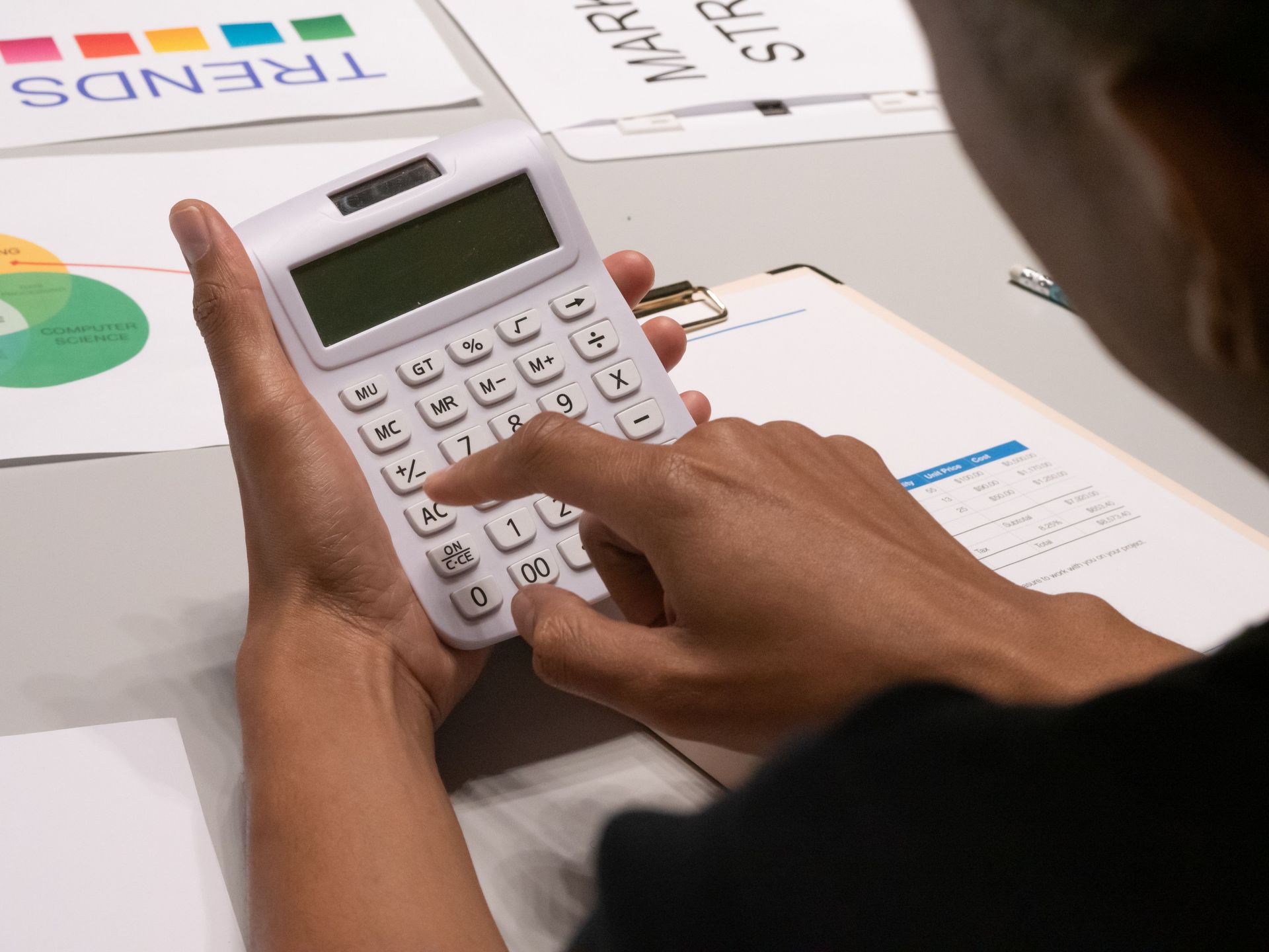 Hands using a calculator on a desk with papers and charts