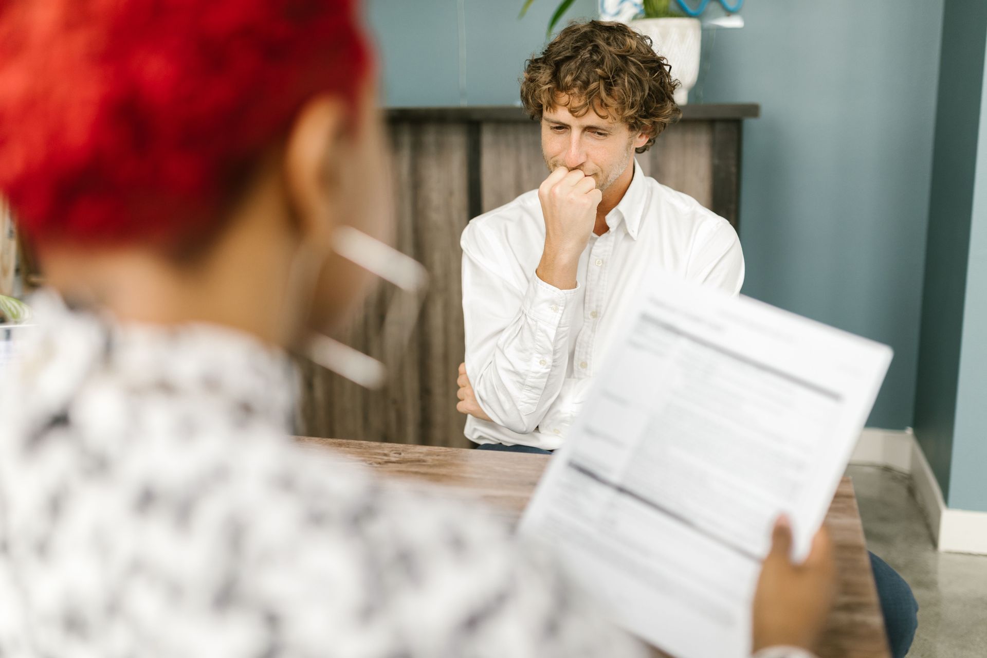 Person in white shirt listening during a counseling session, with another person holding notes in the foreground