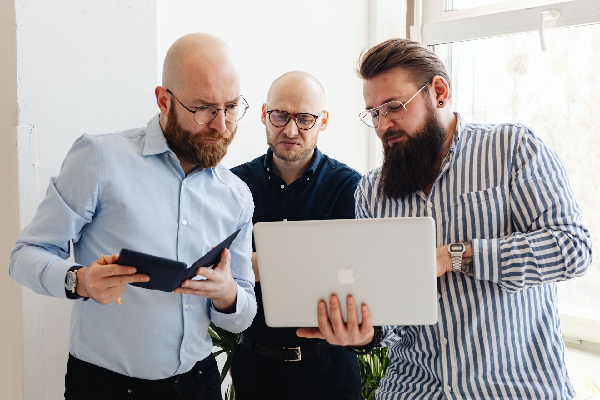 Three people collaborating around a laptop and tablet in a bright office setting